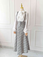 Mannequin wearing a white blouse with a large bow and a black floral dress against a white paneled wall.