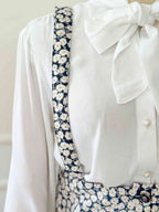 White blouse with a large bow and blue floral patterned straps on a white background