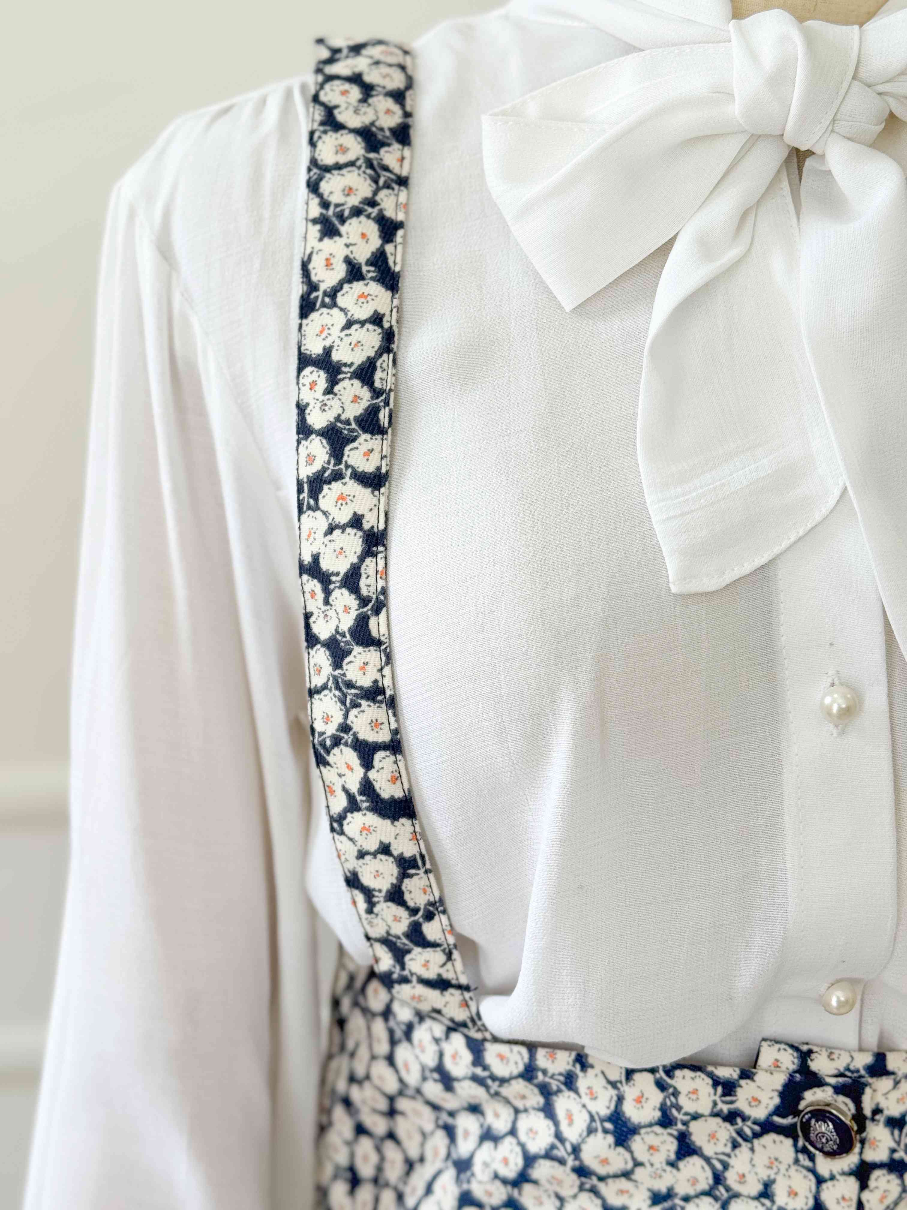 White blouse with a large bow and blue floral patterned straps on a white background