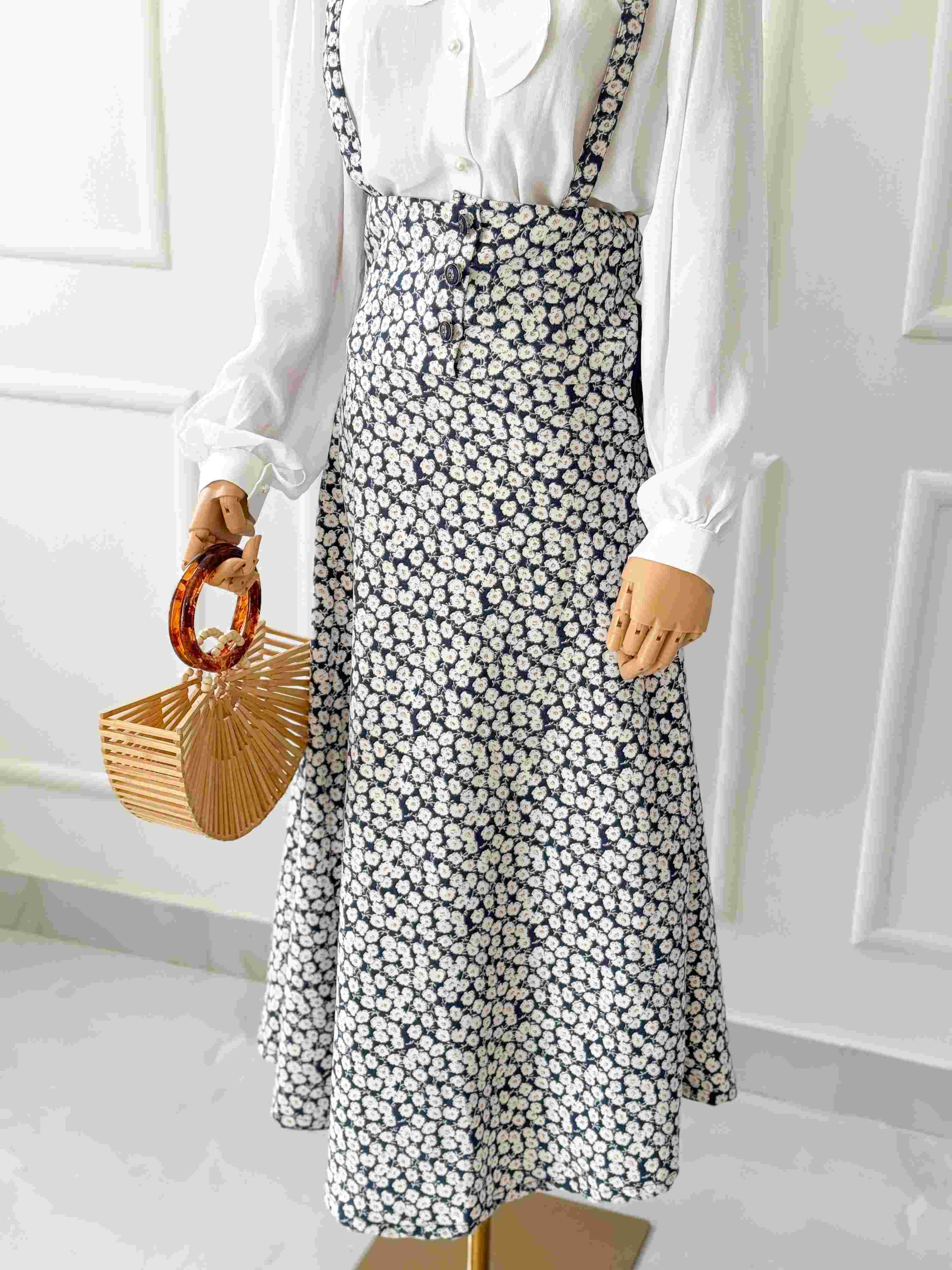 Person wearing a white blouse and black floral skirt holding a small brown bag.