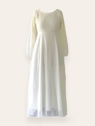 A long off-white dress with a scoop neckline and long, slightly puffed sleeves. The dress features a fitted bodice that transitions into a flowing skirt, with subtle texture detailing on the fabric. The sleeves end in a gentle, elasticized gather.